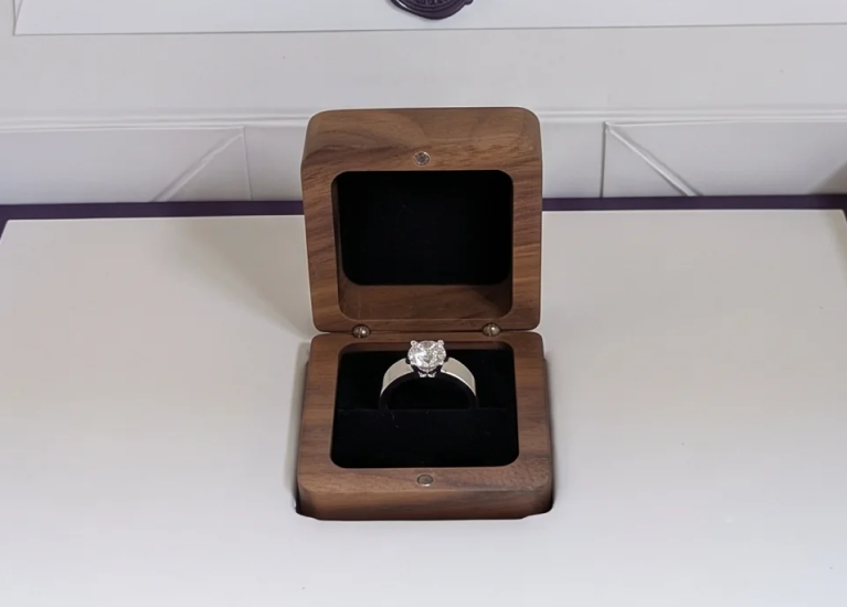 Open SAMA gift box with a wax-sealed envelope and a walnut ring box holding a white gold diamond engagement ring