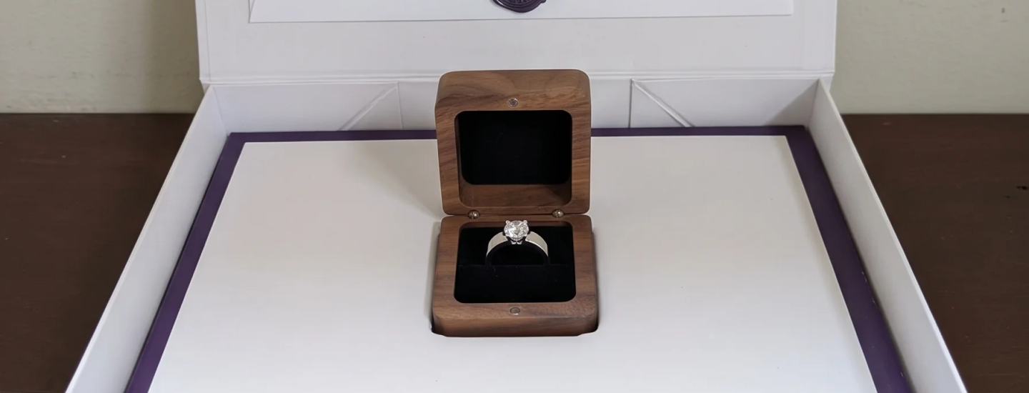 Open SAMA gift box with a wax-sealed envelope and a walnut ring box holding a white gold diamond engagement ring