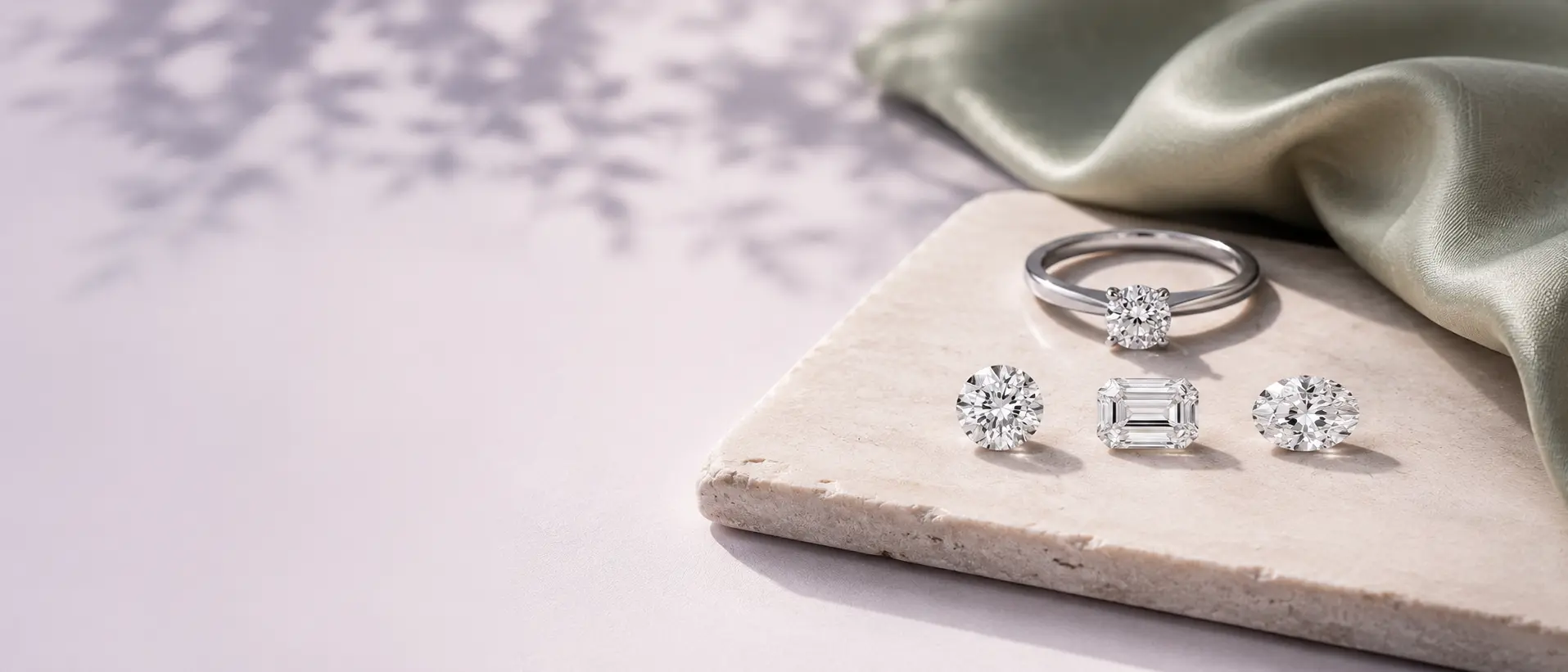 Round brilliant, emerald cut, and oval diamonds beside a solitaire ring on a travertine slab