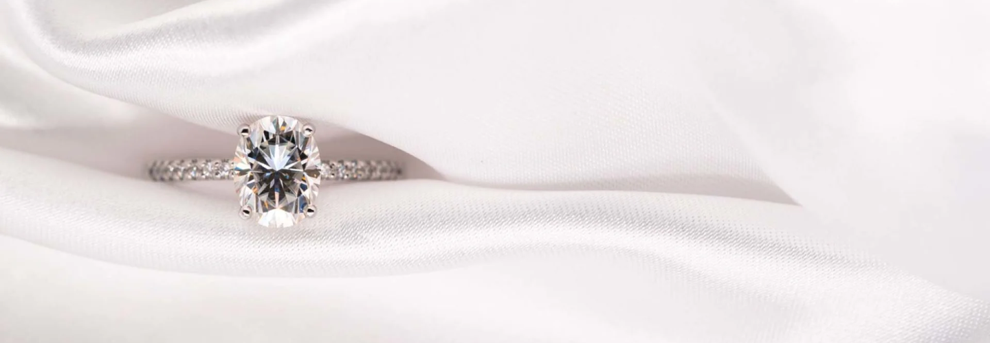 Oval-cut diamond engagement ring on satin fabric by SAMA
