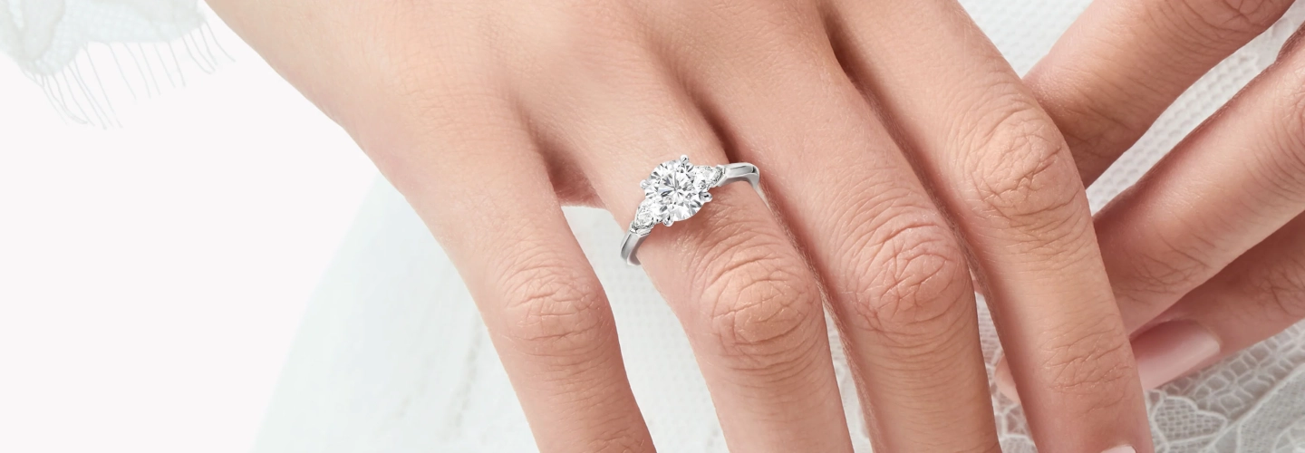 Close-up of a hand wearing a diamond engagement ring with the words “Design your ring. Define your story.” beside it.