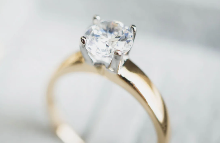 Close-up of a diamond solitaire engagement ring on a yellow gold band with soft holiday lights in the background.