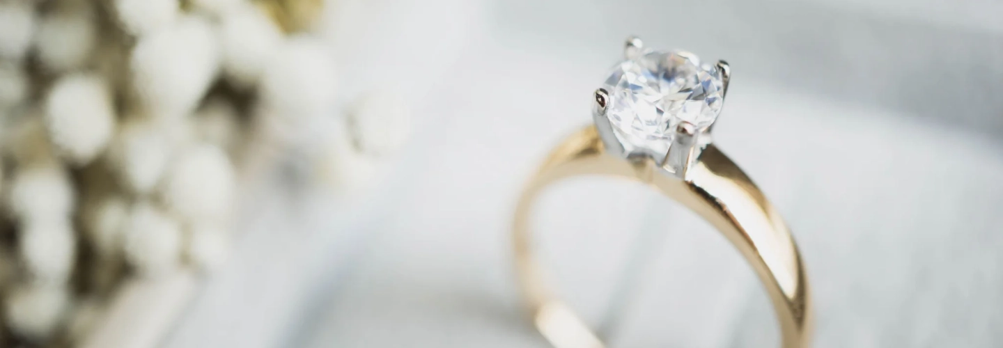 Close-up of a diamond solitaire engagement ring on a yellow gold band with soft holiday lights in the background.