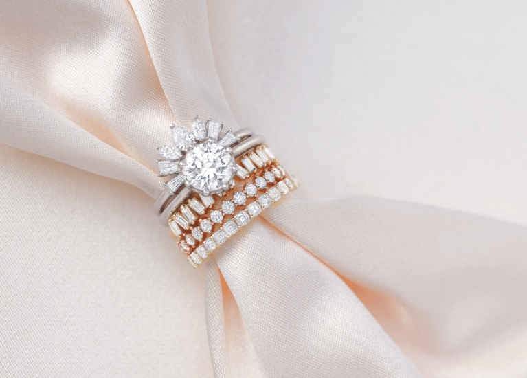 Diamond engagement ring with a half halo of fancy shapes and stacked eternity wedding bands displayed on champagne-colored satin fabric.