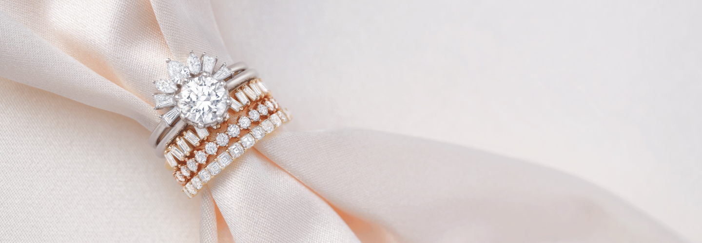 Diamond engagement ring with a half halo of fancy shapes and stacked eternity wedding bands displayed on champagne-colored satin fabric.