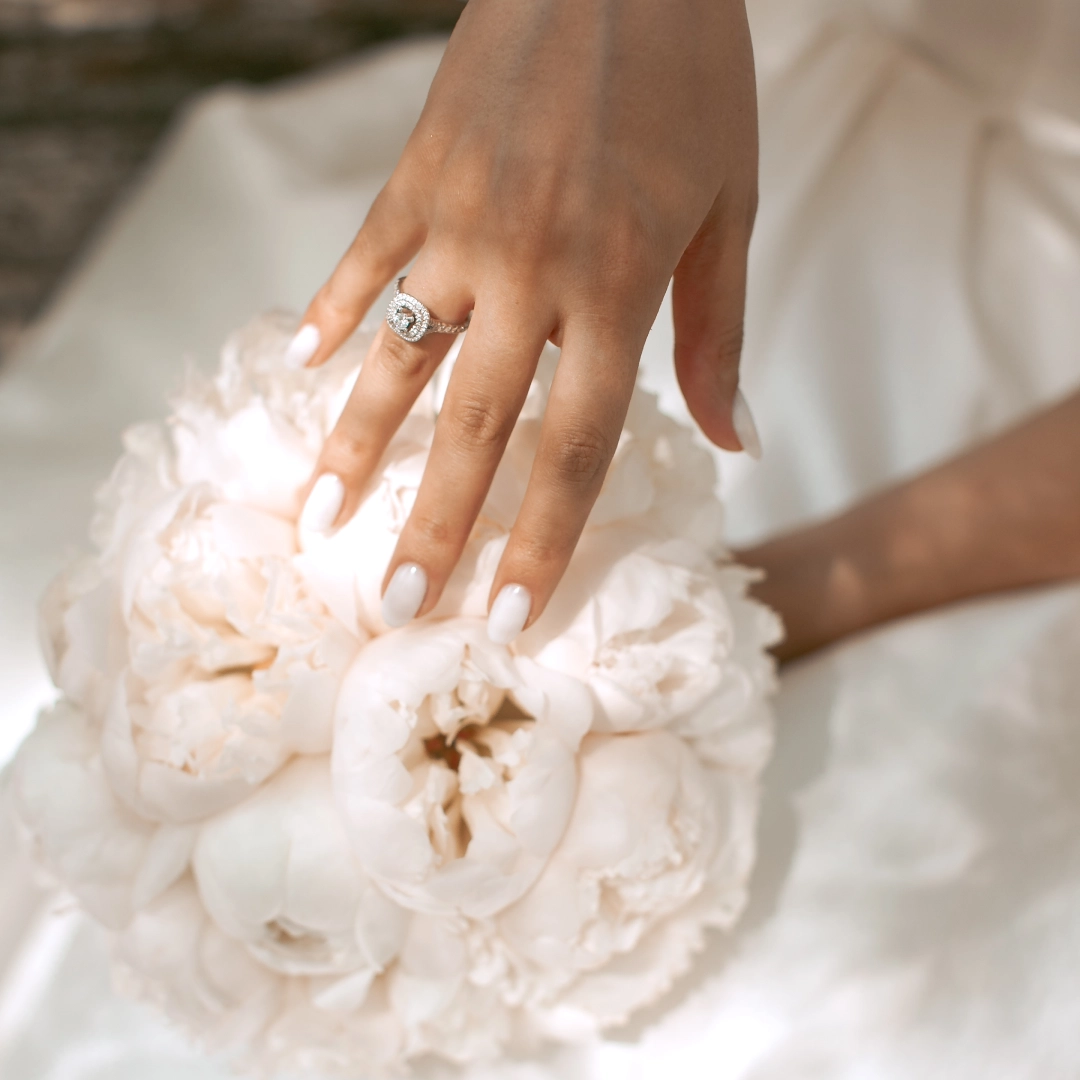 18K white gold halo engagement ring on bride’s hand against bouquet — timeless bridal elegance by SAMA